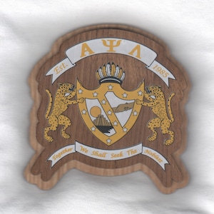 May include: A wooden plaque with a crest featuring a golden sun, stars, and a hand reaching out. Two golden jaguars flank the crest, and the text "AΨΛ Est. 1985" is displayed above. The text "Together We Shall Seek The Noblest" is displayed below the crest.