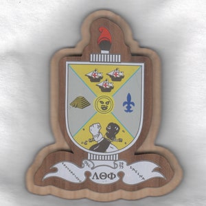 May include: A wooden plaque with a crest featuring a yellow and white shield with a black face, a gold pyramid, and three ships. The shield is surrounded by a blue fleur-de-lis and a black and white figure. The plaque has a brown wooden background with the text "LOF" and "DEC 19 75" in white.