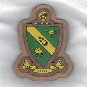 May include: A wooden plaque with a green and yellow shield, a tree, a crescent moon, three stars, and a lamp. The shield is surrounded by a scroll with the words "Alpha Gamma Rho" in Greek letters.