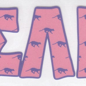 May include: Pink letters spelling out the Greek letters ΣAT, with a purple outline. The letters are filled with a pattern of running purple cheetahs. The background is white.
