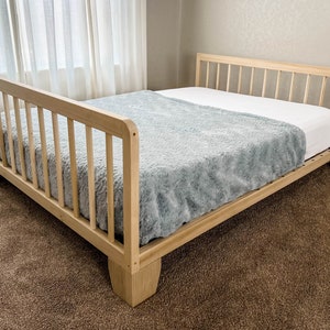 May include: A wooden bed frame with a light wood finish and a gray blanket on top. The bed frame has a slatted headboard and footboard.