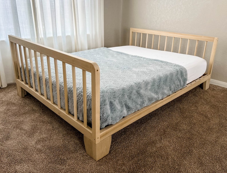 May include: A wooden bed frame with a light wood finish and a gray blanket on top. The bed frame has a slatted headboard and footboard.