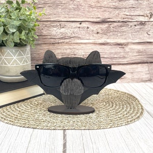 May include: A black wooden bat with sunglasses, a carved pumpkin face, and a wooden stand. The bat is wearing black sunglasses.