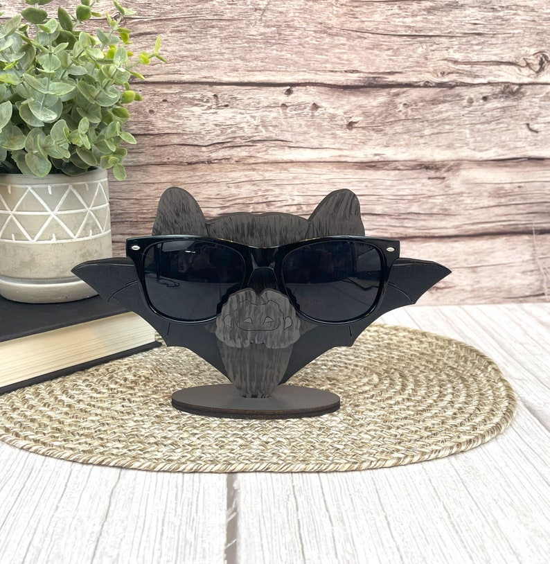 May include: A black wooden bat with sunglasses, a carved pumpkin face, and a wooden stand. The bat is wearing black sunglasses.