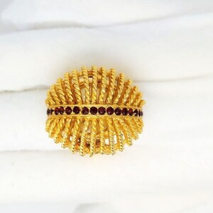 May include: A gold ring with a woven design and a band of dark red stones.