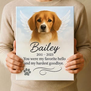 A person in a beige sweater holding the pet memorial canvas featuring a golden dog with angel wings and the quote about saying goodbye, showing the scale and detail of the product.