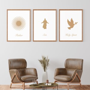 May include: Three framed art prints with a religious theme. Each print features a gold-colored illustration on a white background. The prints depict a sunburst, a figure with outstretched arms, and a dove with an olive branch. The words "Father", "Son", and "Holy Spirit" are below each image.
