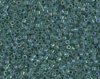 May include: A close-up view of a pile of small, cylindrical beads. The beads are a translucent teal color with a subtle iridescent sheen. They are densely packed together, filling the frame.