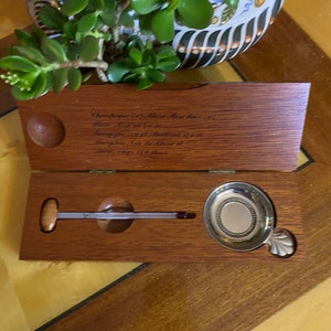 以下が含まれることがあります： 木製の箱の中に銀の皿と温度計が入っています。箱には「シャンパン1967年、白ワイン、親愛なる...」という刻印があります。