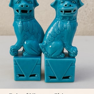 May include: A pair of turquoise Foo Dog statues. Each dog is seated atop a square base with decorative cutouts. The statues are 12 cm tall and feature detailed carvings, including flowing manes and ornate collars.