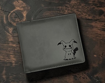 Op de afbeelding: Een rechthoekige grijze portemonnee met twee vouwen, voorzien van een zwarte, lasergegraveerde afbeelding van het personage Mimikyu in de rechterbenedenhoek. De portemonnee heeft strakke randen en een gladde, matte afwerking.