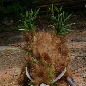 May include: A brown furry creature with green leafy branches on top of its head. The creature is standing on a dirt and brick surface.
