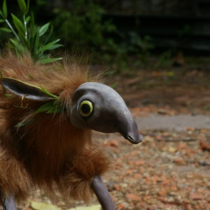 May include: A brown and gray furry creature with a long snout and large eyes. The creature has green leaves and twigs in its fur.