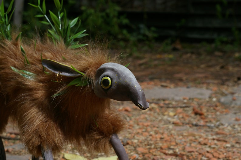May include: A brown and gray furry creature with a long snout and large eyes. The creature has green leaves and twigs in its fur.