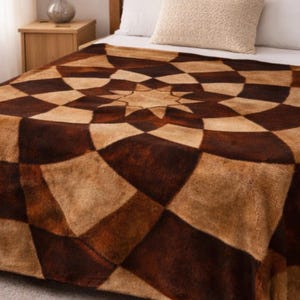 May include: A plush blanket featuring a geometric starburst pattern in alternating shades of dark brown and light tan. The soft-textured throw is draped over a bed, displaying a repeating diamond and curved shape design that radiates from the center.