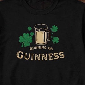 Funny Running on Guinness St Patrick’s Day shirt featuring a beer mug and shamrock design printed on Gildan 5000 unisex t shirts available in black white Irish green and antique Irish green colors, humorous Irish drinking shirt perfect for St Paddy’s Day pub crawls parties festivals and Irish holiday celebrations.