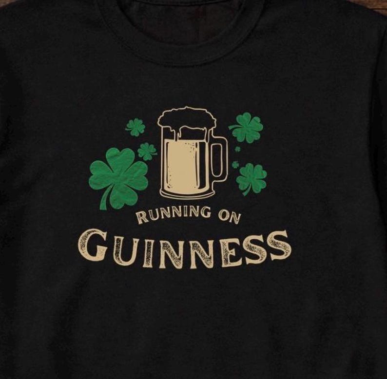 Funny Running on Guinness St Patrick’s Day shirt featuring a beer mug and shamrock design printed on Gildan 5000 unisex t shirts available in black white Irish green and antique Irish green colors, humorous Irish drinking shirt perfect for St Paddy’s Day pub crawls parties festivals and Irish holiday celebrations.