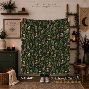 May include: A plush blanket measuring 50 inches by 60 inches, featuring a dark green background with a repeating pattern of white mushrooms, green ferns, pink foxglove flowers, and small dragonflies printed across the fabric surface.