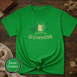 Funny Running on Guinness St Patrick’s Day shirt featuring a beer mug and shamrock design printed on Gildan 5000 unisex t shirts available in black white Irish green and antique Irish green colors, humorous Irish drinking shirt perfect for St Paddy’s Day pub crawls parties festivals and Irish holiday celebrations.