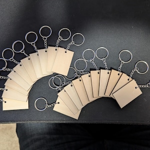 May include: A set of 18 blank wooden keychains with silver key rings. The keychains are arranged in a semi-circle shape.