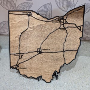 May include: A wooden map of the state of Ohio with the major cities labelled. The cities labelled are Toledo, Cleveland, Akron, Columbus, Dayton, and Cincinnati.
