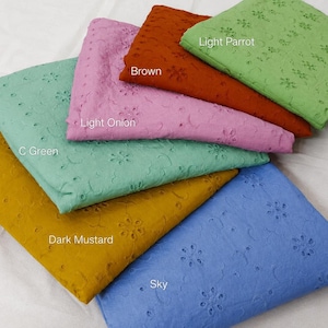 May include: A collection of six folded fabric swatches featuring eyelet embroidery with floral patterns. The colors are labeled as Light Parrot, Brown, Light Onion, C Green, Dark Mustard, and Sky. Each piece of fabric displays a consistent cut-out design.