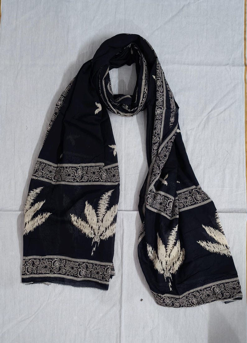 May include: A dark navy blue scarf with a white floral and leaf pattern. The scarf has a decorative border with a repeating design. The scarf is made of a lightweight fabric and is suitable for various occasions.