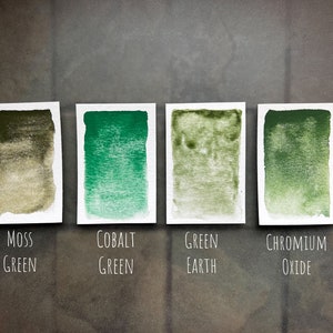 May include: Four watercolor paint swatches on white paper cards. The swatches are labeled "Moss Green", "Cobalt Green", "Green Earth", and "Chromium Oxide".