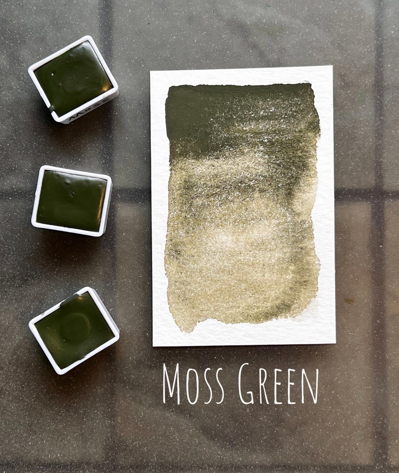 May include: Three watercolor paint pans with a green pigment labeled "Moss Green". The paint is a dark green with a lighter green gradient.