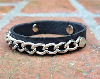 May include: A black leather bracelet with a silver chain detail. The bracelet has two silver snaps.