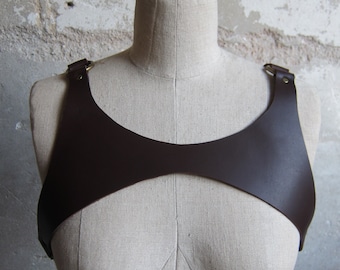May include: A brown leather harness with gold metal rings. The harness is worn on a mannequin.