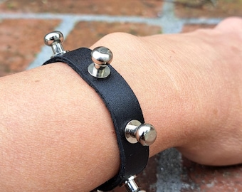 May include: A black leather bracelet with silver studs. The bracelet is worn on a person's wrist.