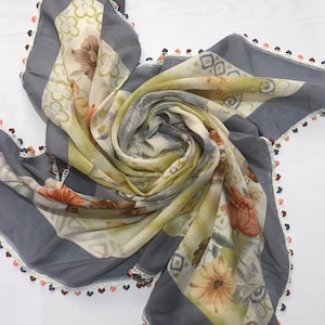 May include: A gray and white floral patterned scarf with a crocheted trim in white, pink, and brown.