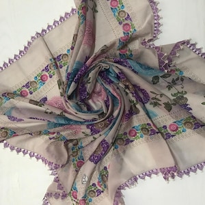 May include: A beige scarf with a floral print and purple crocheted trim. The scarf is made of a lightweight fabric and has a delicate feel.