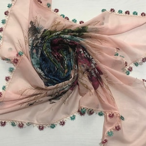 May include: A light pink square scarf with a floral design in the center. The scarf has a delicate, scalloped edge with alternating burgundy and teal floral accents. The center features a colorful, abstract floral pattern.