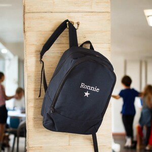 May include: A navy blue backpack with a white star and the name "Ronnie" embroidered on the front.