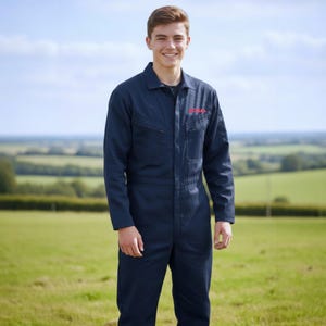 May include: A navy blue jumpsuit with a collared neckline and a zipper closure. The jumpsuit has a pocket on the chest with red text. The person is standing in a field with a green landscape and a blue sky.