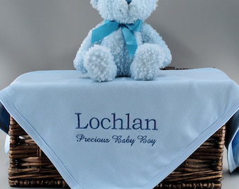 May include: A light blue baby blanket with the name "Lochlan" and the text "Precious Baby Boy" embroidered in dark blue thread. A light blue teddy bear with a light blue ribbon is sitting on top of the blanket.