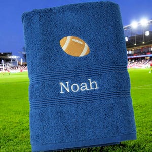 Könnte beinhalten: Blaues Badetuch mit einem weißen gestickten Fußball und dem Namen "Noah" in weiß.