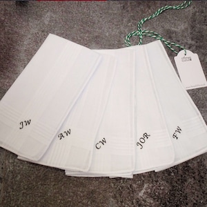 Pode incluir: Cinco lenços brancos com diferentes iniciais bordadas. As iniciais são "JW", "AW", "CW", "JOR" e "FW".