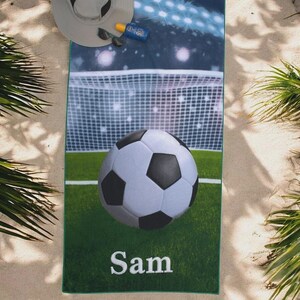 Könnte beinhalten: Ein rechteckiges Strandtuch mit einem Aufdruck eines Fußballfeldes, eines Tornetzes und eines großen schwarz-weißen Fußballs. Der Name Sam ist unten in weißen Buchstaben aufgedruckt. Das Tuch hat einen dunkelgrünen Rand und eine glatte Oberfläche.