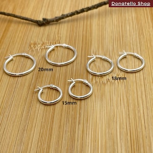 May include: Four silver hoop earrings of different sizes on a wooden surface. The earrings measure 15mm, 18mm, and 20mm in diameter.