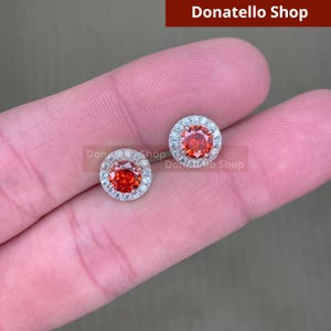 May include: A pair of silver stud earrings with a red gemstone surrounded by a halo of smaller white gemstones.