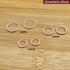 May include: A set of six silver hoop earrings in three different sizes: 10mm, 12mm, and 14mm. The earrings are arranged in a row on a wooden surface.