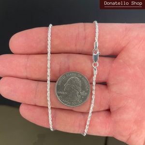 May include: A silver rope chain necklace with a lobster clasp. The chain is shown next to a US quarter for size reference.