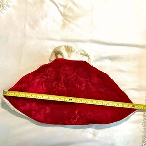 May include: A red velvet Christmas stocking with a white faux fur trim. The stocking is measured with a yellow tape measure, showing a length of approximately 24 inches.