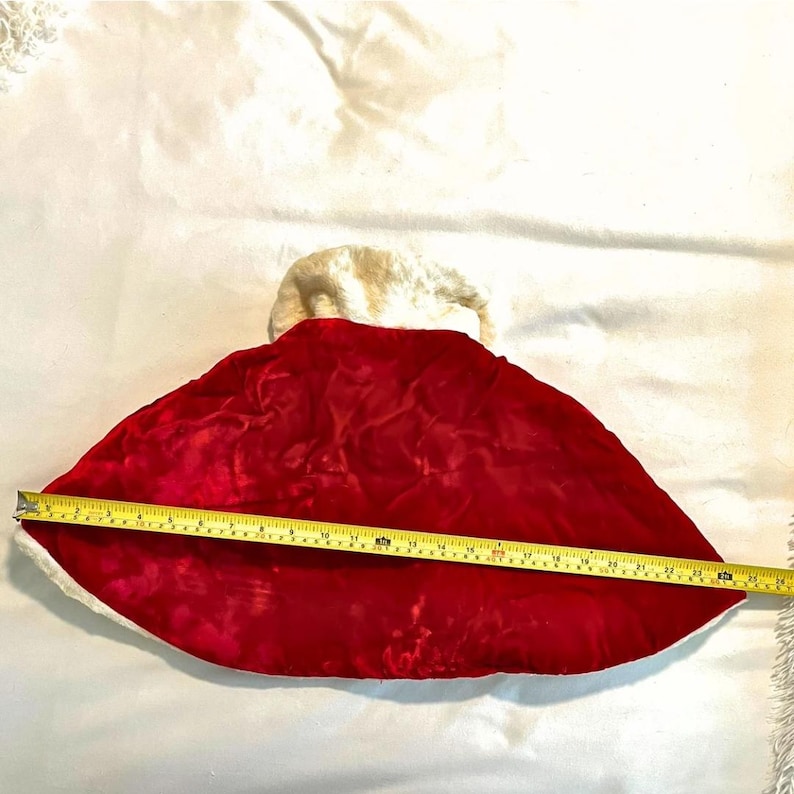 May include: A red velvet Christmas stocking with a white faux fur trim. The stocking is measured with a yellow tape measure, showing a length of approximately 24 inches.