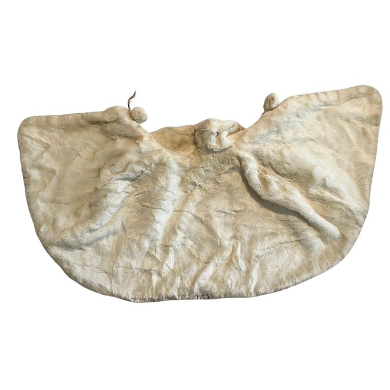 May include: A cream-colored, textured sculpture with a rounded shape. The artwork features three figures with outstretched arms, resembling wings. The piece has a soft, organic appearance, with subtle variations in tone and texture.