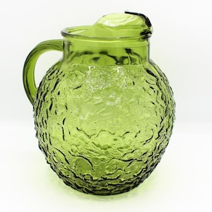 May include: A green glass pitcher with a textured surface and a lid. The pitcher has a round body and a handle.