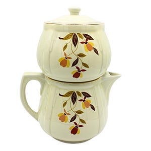 May include: Cream-colored vintage teapot and sugar bowl set. The teapot has a handle and spout, and the sugar bowl has a lid. Both pieces are decorated with a floral pattern in brown, yellow, and red.
